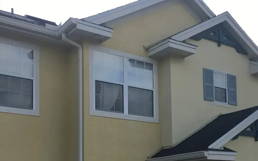 A clean white gutter running the length of the eave on a two storey stucco building, with the downspout turning down at the corner